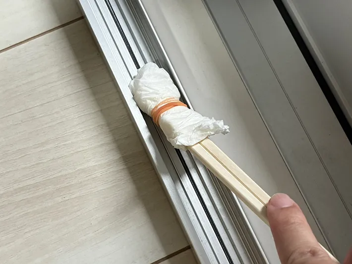 キッチンペーパーをつけた割り箸でサッシを掃除する場面（撮影：grapeライフハック編集部）