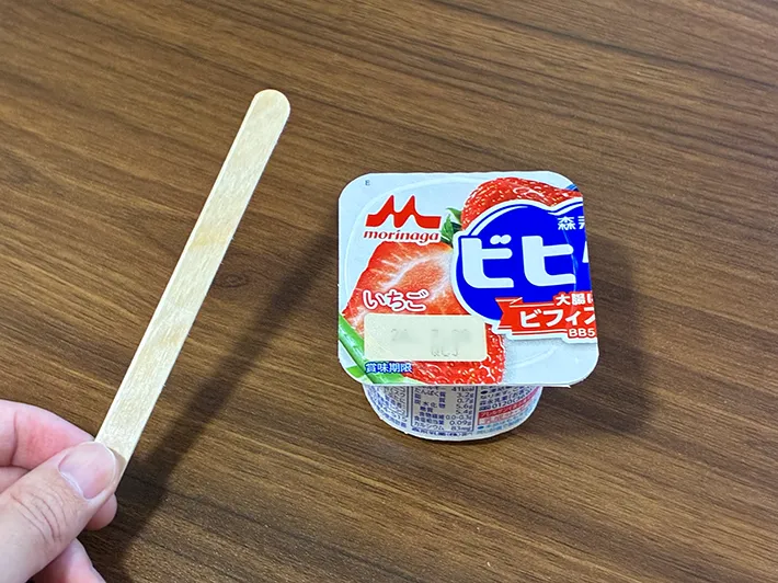 机に置かれたヨーグルトと、手で持ったアイスの棒（撮影：grapeフード編集部）