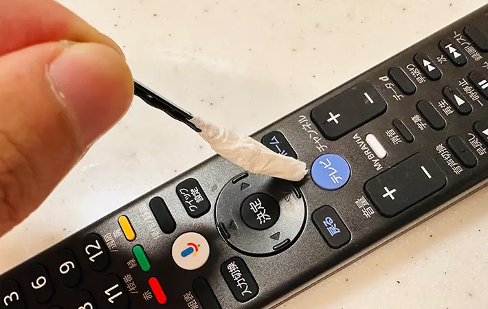 ヘアピンの先にティッシュを巻いてテレビリモコンのボタンの隙間を掃除している写真（grapeライフハック編集部）