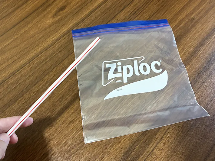 机に置かれたジッパー袋と、手で持ったストロー（撮影：grapeライフハック編集部）