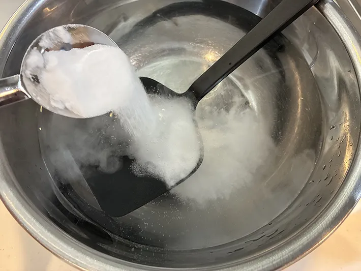 お湯とシリコン製調理器具が入った容器に重曹を入れる場面（撮影：grapeライフハック編集部）