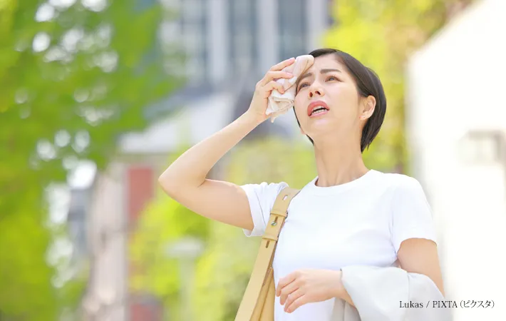 『額の汗をハンカチで拭き陽射しを気にする女性』の写真