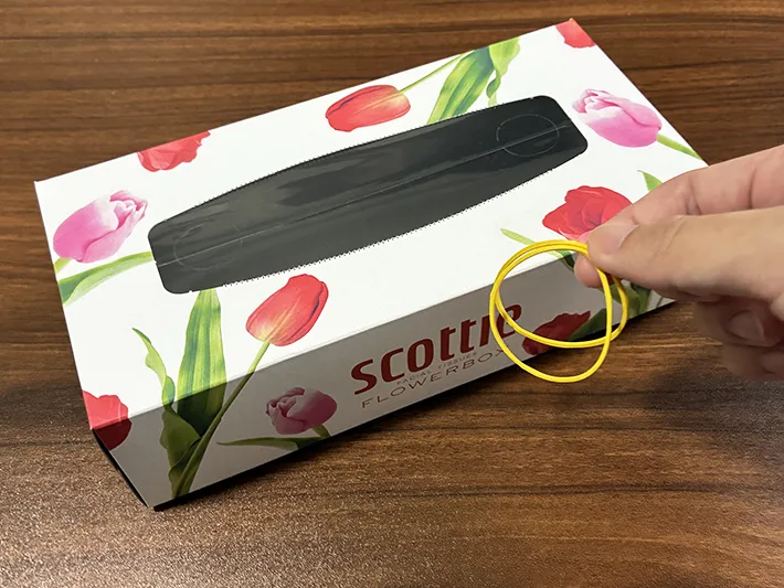 机に置いたティッシュの空き箱と、指で持った輪ゴム（撮影：grapeライフハック編集部）