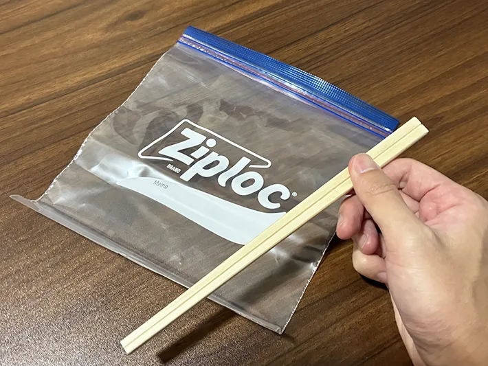 机に置いたジッパー袋と、手で持った割り箸（撮影：grapeライフハック編集部）