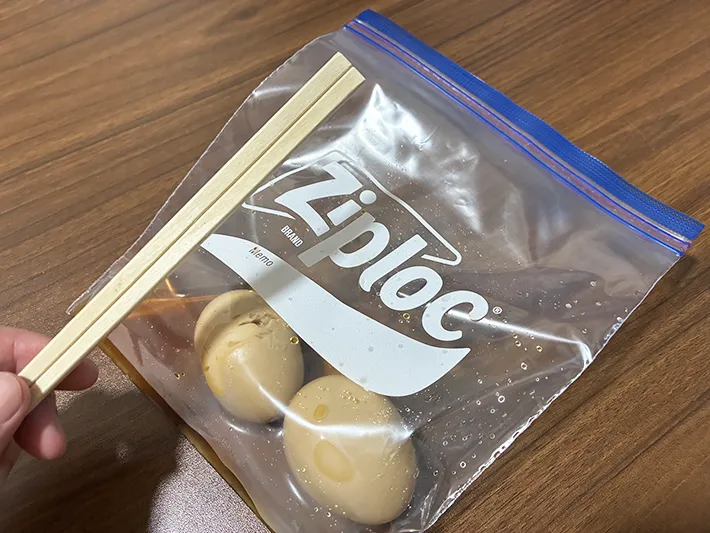 味玉を入れたジッパー袋と、手で持った割り箸（撮影：grapeライフハック編集部）