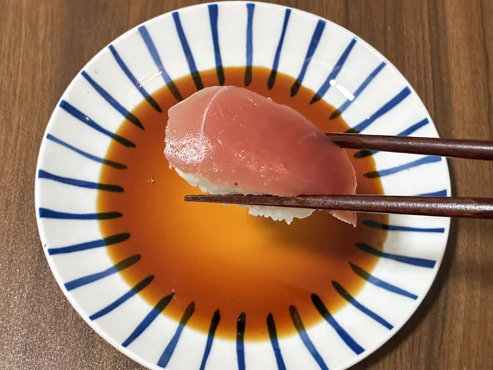 箸でつかんだ、ラップと新聞紙で包んで保存したマグロの寿司（撮影：grapeフード編集部）