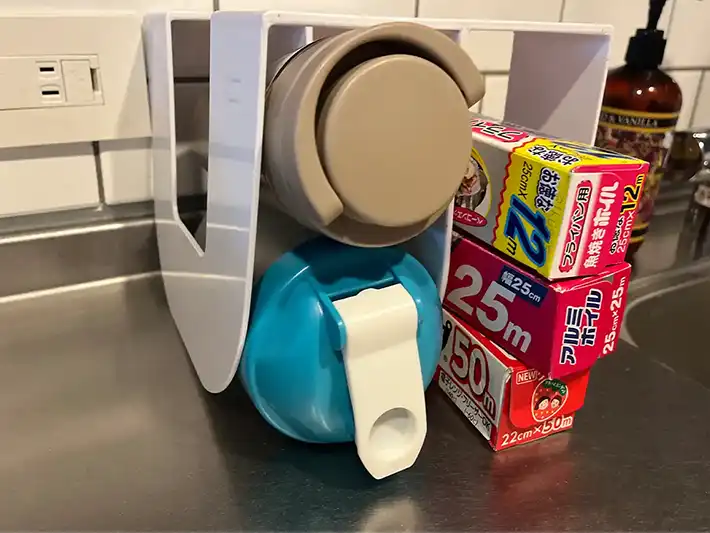 ブックスタンドで水筒やプロテインシェイカー、アルミホイルなどの箱を整理した様子（撮影：grapeライフハック編集部）