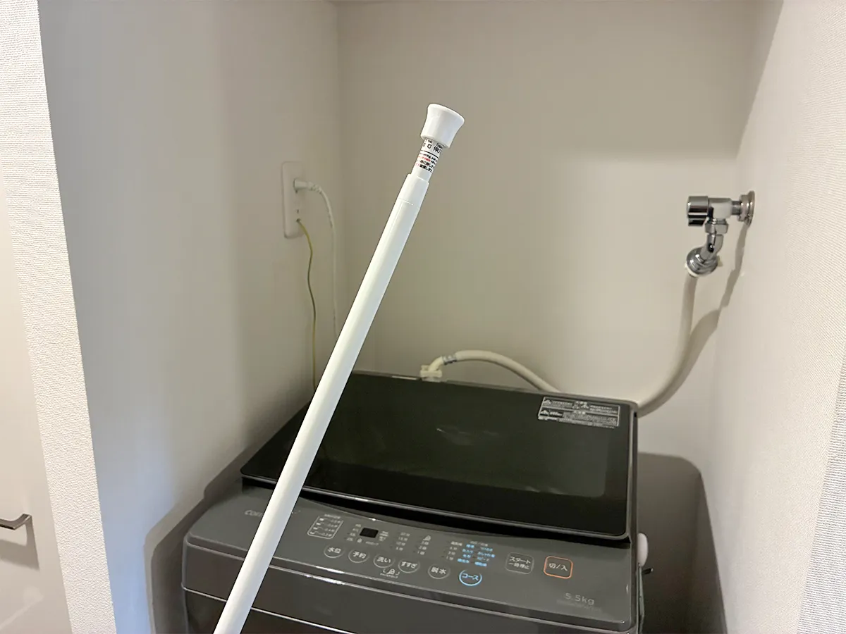 洗濯機そばで手にするつっぱり棒(撮影:grapeライフハック編集部)